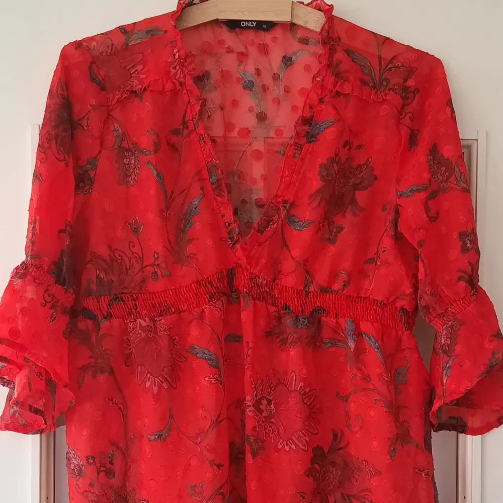 Colourful red blouse with flowers, dots and a sheer material - perfect for the summer! 100% polyester . Blusar.