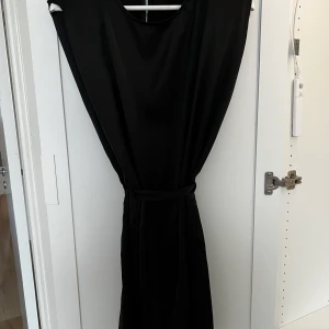 Silkesklänning - Svart armlös silkesklänning med mindre axelvaddar samt bälte i midjan, oanvänd