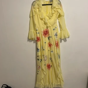 Gul blommig maxiklänning  - Gul maxiklänning med broderade blommor och volanger. Supersöt sommarklänning i chiffon material. Helt ny aldrig använd. Slits finns. Från ASOS. 