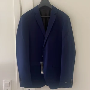 Blå Jack & Jones kostym knappt använd - Jag säljer min kostym som blivit för liten. Kavajen är aldrig använd där prislappen sitter kvar och byxorna är använda en gång.  Säljer på grund av att det är för litet för mig. Ordenarie pris ligger på 979kr 