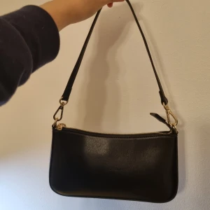Svart axelremsväska - En jättefin och trendig svart axelremsväska från brandy melville :)! Köpte för 330 kr och frakt, använd endast en gång då den inte är riktigt min stil ;(. Nästan helt ny och felfri 💕 Den söker ett nytt hem som kan styla den fint <3 
