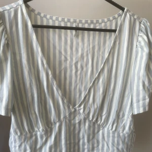 V-ringad topp - Supersöt vit- och blårandig topp med v-ringning. Lite puffiga ärmar som är korta. Använd ett fåtal gånger.  Köparen står för frakten!