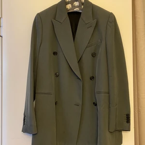 Kavaj från Tiger of Sweden.  - Superfin kavaj från Tiger of Sweden i vacker grön färg. Lite glansigt material vilket ger en lyxig finish. Dubbelknäppt med svarta knappar. Storlek 38 som passar 36-38 beroende på hur oversize du vill att den ska sitta. Toppenskick. Inköpt för ca 4000kr.