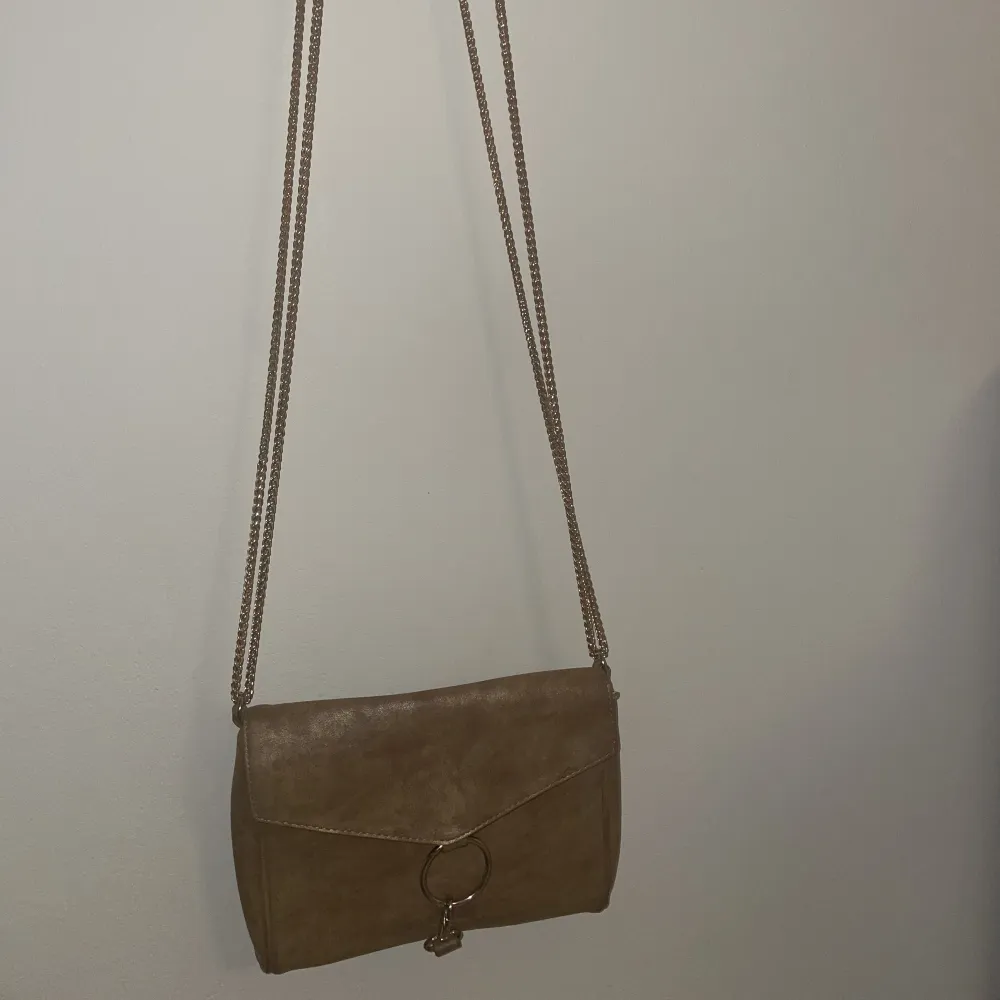 En handväska från gina tricot. Den är i färgen brun/guldinslag som syns bättre på andra bilden som är tagen med blixt. . Väskor.