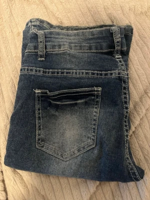 Mörkblå jeans med slitningar - Snygga mörkblå jeans med ljusa slitningar och klassisk femficksdesign. Jeansen har normal midja, bälteshällor och utsvängda ben. Materialet är denim med tydliga kontrastsömmar. Perfekta vardagen — osäker på vart dom är ifrån. 🩷