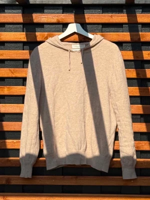 Sayless Kashmir hoodie  - Säljer en stilren beige Kashmir hoodie med huva och dragsko. Hoodien har långa ärmar, ribbade muddar och är gjord i ett mjukt, stickat material som känns riktigt skönt mot huden.