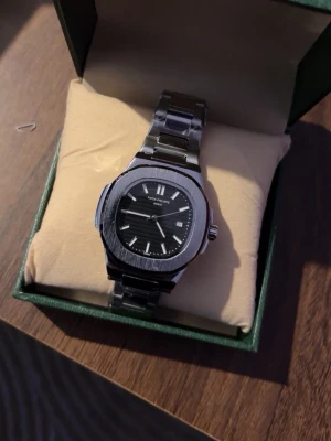 Klocka - Stilren klocka med svart urtavla och silverfärgat armband i metall. Klockan har datumvisning och klassisk design med rektangulär boett och länkarmband. Perfekt accessoar för dig som gillar exklusiv stil.