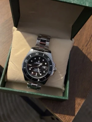 Klocka - Klassisk klocka med svart urtavla och svart vridbar bezel. Armbandet är i rostfritt stål och klockan har tydliga vita markeringar och visare. Perfekt för dig som gillar tidlös och sportig design.
