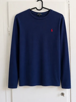Polo Ralph Lauren långärmad tröja – marinblå 🔵🔴 - Klassisk långärmad tröja från Polo Ralph Lauren i marinblått med den ikoniska röda broderade Polo-loggan på bröstet.  • Storlek M (10–12), junior • Marinblå med röd broderad logga • Långärmad modell • Rund hals • Stilren och lättmatchad • Fint begagnat skick utan defekter!  Perfekt som basplagg till vardags. Skriv gärna vid frågor eller om du vill ha mått 📦