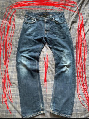 Nudie jeans  - Säljer ett par klassiska blå jeans med raka ben och snygga slitningar på framsidan. Jeansen har fem fickor, normal midja och kontrastsömmar. Perfekta för en avslappnad och trendig look. Materialet är denim i bomull.