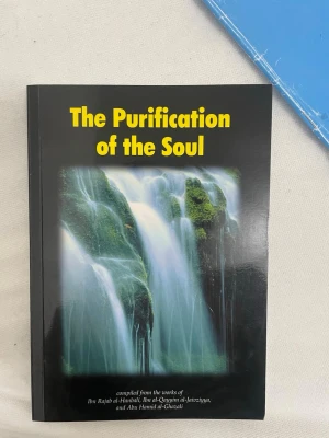 The Purification of the Soul bok - En bok med titeln 'The Purification of the Soul' med svart omslag och ett motiv av ett vattenfall med gröna mossiga stenar. Texten på framsidan är i gul färg. Boken är på engelska och utgiven av Al-Firdous Ltd.