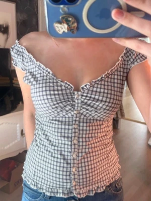 Rutig offshoulder topp med knappar - Supersöt rutig topp i vitt och blått med offshoulder-modell och volangkant. Använd en gång