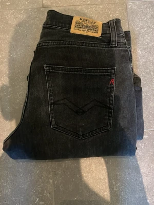 Svarta Replay jeans 158cm - Säljer ett par svarta jeans från Replay med klassisk femficksmodell och raka ben. Jeansen har en snygg tvätt, läderpatch bak i midjan och diskret röd detalj på bakfickan. Perfekta för dig som gillar stilrena och tidlösa jeans.