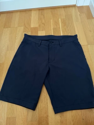 Mörkblå shorts peak performance  - Snygga mörkblå shorts med knapp och dragkedja framtill samt två sidofickor. Golfshorts som passar perfekt till sommaren.