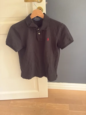 Ralph lauren pike - Klassisk svart pikétröja från Polo Ralph Lauren med korta ärmar och röd broderad logga på bröstet. Slim fit-modell med krage och två knappar framtill. Perfekt till jeans eller shorts för en clean och stilren look.
