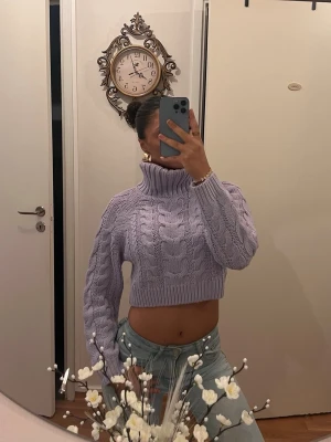 Ljuslila cropped kabelstickad polotröja - Säljer en ljuslila cropped stickad tröja med polokrage och kabelstickat mönster. Tröjan har långa ärmar och ribbade muddar. Perfekt för dig som vill ha en trendig och mysig look i höst och vinter.