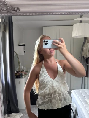 Vit omlott halterneck linnetopp - Säljer en superfin vit linnetopp med halterneck och omlott framtill. Toppen har volangdetaljer och är ärmlös, perfekt för sommardagar. Materialet känns lätt och luftigt, och toppen har en snygg v-ringning.