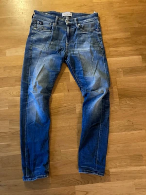 Blå slim fit jeans från Calvin Klein - Snygga blå slim fit jeans från Calvin Klein med klassisk femficksdesign och diskreta slitningar framtill. Jeansen har en CK-logga på bakfickan och är tillverkade i denim med stretch för extra komfort.