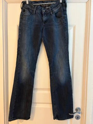 Blåa Lågmidjade bootcut jeans - Säljer ett par blå bootcut lowwaist jeans. Jeansen har låg midja och subtila detaljer på bakfickorna. Materialet är denim med en skön tvättad look. 