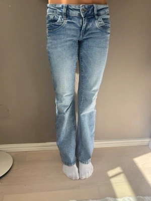 Ljusblå bootcut jeans - Säljer ett par ljusblå bootcut jeans med klassisk femficksdesign och normalhög midja. Jeansen har en snygg tvättad look och är tillverkade i denim med lite stretch för skön passform. Perfekta till en avslappnad stil.