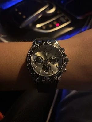 Stilren silverfärgad klick  - Snygg kronografklocka med silverfärgad urtavla och svart boett. Klockan har tre mindre urtavlor, tydliga markeringar och svart armband. Perfekt accessoar för dig som gillar en sportig men ändå klassisk look.
