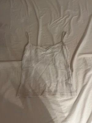 Ljusribbad linnetopp med smala band - Säljer en ljus, ribbad linnetopp med smala axelband och lätt v-ringad hals. Toppen är croppad och har en enkel, stilren look som passar perfekt till jeans eller kjol.