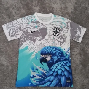 Brasil fotbolls tröja - Unik t-shirt med korta ärmar och ett stort tryck av en blå papegoja framtill. T-shirten har coola grafiska detaljer i vitt, grått och turkost samt en logga på bröstet. Tillverkad i mjukt material, perfekt för dig som gillar att sticka ut.