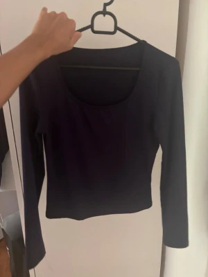 Mörkblå långärmad topp med rund hals - En enkel och stilren mörkblå långärmad topp med rundad halsringning. Perfekt att matcha med jeans eller kjol för en clean look. Materialet känns mjukt och stretchigt, vilket gör den bekväm att bära hela dagen.