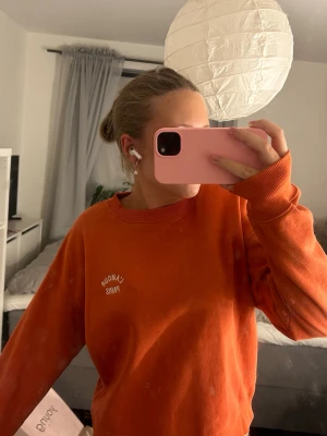 Orange sweatshirt  - Snygg orange sweatshirt med trycket 'L'AMOUR PARIS' i vitt på bröstet. Tröjan har rund halsringning, ribbade muddar vid ärmslut och nederkant samt en avslappnad passform. Perfekt för en chill och trendig look. Den är som ny, den är använd 2-3 gånger max och har verkligen inga tecken på användning. 