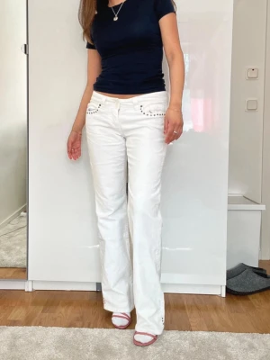 Vita raka jeans  - Säljer ett par vita jeans med rak passform och snygga silverfärgade nitar vid fickorna. Jeansen har klassisk femficksdesign och normal midja. Perfekta för dig som vill sticka ut med en fräsch och trendig look.