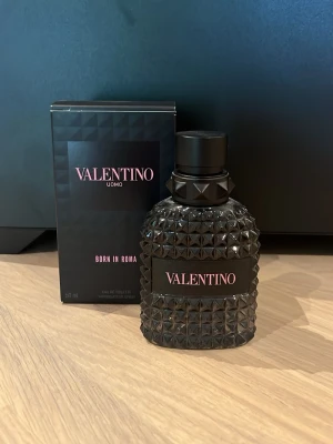 Valentino Uomo Born In Roma EdT 50ml - Valentino Uomo Born In Roma är en elegant herrparfym i en svart, nitat glasflaska med matchande svart lock. Flaskan har en lyxig och modern design med rosa detaljer på etiketten. Förpackningen är svart med rosa text och geometriskt mönster. 50 ml flaska men är ungefär 40 ml kvar🙌🏼