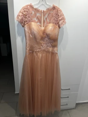 rosafärgad festklänning - Säljer en elegant klänning med korta spetsärmar och vackra spetsdetaljer över bröstet och ryggen. Klänningen har en markerad midja och ett flowy, kjolparti i tyll. Perfekt för speciella tillfällen! Aldrig använd då den satt för stor. Köpt för 2000kr