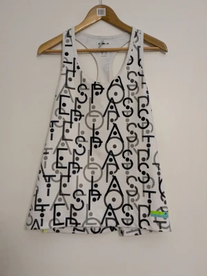 Träningslinne Adidas x Stella McCartney  - Säljer ett jättefint och skönt träningslinne från samarbetet mellan Adidas och Stella McCartney (StellaSport). Vitt med ett coolt, grafiskt mönster i svart och grått, samt snygga neongula detaljer i sprunden nertill på sidorna. Linnet är i klassisk brottarrygg-modell (racerback) och tillverkat i Adidas fukttransporterande Climalite-material som håller dig torr under passet.  Etiketten är avklippt.
