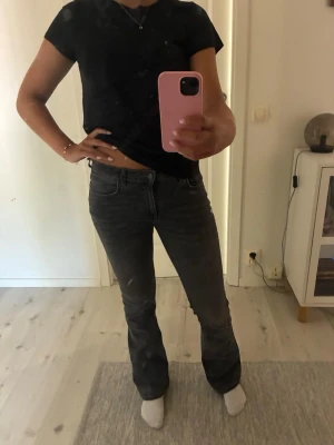 Mörkgrå bootcut jeans - Säljer ett par mörkgrå bootcut jeans med klassisk femficksmodell och normal midja. Jeansen har en lätt utsvängd passform nedtill och stängs med dragkedja och knapp. Perfekta till en avslappnad och trendig look.