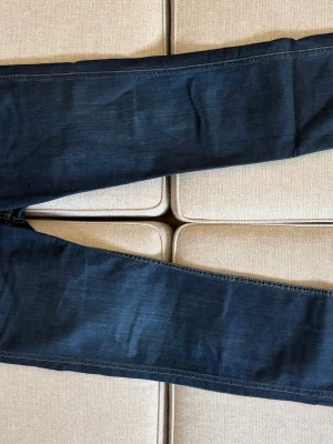 Mörkblå slim fit jeans från boss - Säljer ett par mörkblå slim fit jeans med klassisk femficksdesign och dragkedjegylf. Jeansen har snygga kontrastsömmar och detaljer i kopparfärg. Materialet är stretchigt denim som ger en bekväm passform.