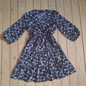 New Look Blommig Klänning med Volang - Söt kort klänning med blommigt mönster från New Look Petite. Klänningen har trekvartsärmar med resår. Klänningen är i väldigt fint skick och knappt använd.                                                              Byst ca 86 cm.                                                 Midjan är elastisk med resår.                             Längd ca 81 cm.