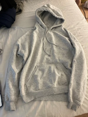 Ljusgrå hoodie från BikBok - Ljusgrå hoodie från BikBok med klassisk huva och dragsko. Hoodien har en stor magficka och ribbade muddar vid ärmslut och nederkant. Tillverkad i mjukt sweatshirtmaterial som är perfekt för chill dagar.