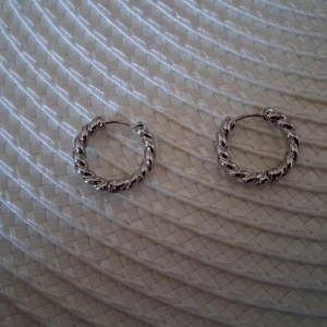 Silverfärgade Tvinnade Creoler - Ett par örhängen i form av små creoler med tvinnad design. Diameter ca 2,8 cm. Nya och oanvända men saknar förpackning och prislapp.