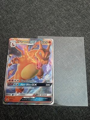 Charizard (GX) Pokémonkort - Säljer ett Charizard GX Pokémonkort med 250 HP och är GX. Kortet har en färgstark design med Charizard i orange och blått, och är tryckt på glansigt pappmaterial. Perfekt för samlare eller Pokémonfans! Ges även med en plastficka.