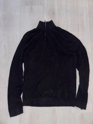 Svart halvzip tröja från Topman - Svart långärmad tröja från Topman med halvzip och hög krage. Tröjan är i ett mjukt stickat material och har ribbade muddar vid ärmslut och nederkant. Perfekt för en stilren och enkel look.