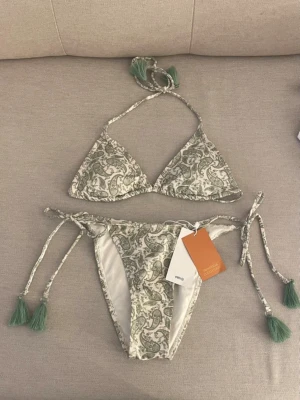 Grön paisley bikini från MNG - Snygg bikini från MNG med paisley-mönster i grönt och vitt. Både överdel och underdel har knytband med gröna tofsar. Perfekt för stranden eller poolen, och bikinin har en klassisk trekantsmodell. Nypris 429kr och den finns inte att köpa längre 
