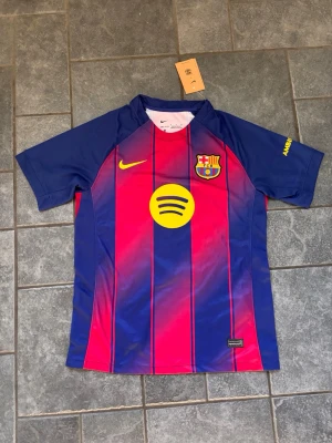 Barcelona matchtröja Nike röd/blå S - Säljer en officiell FC Barcelona matchtröja från Nike i röd och blå med gula detaljer. Tröjan har klubbmärke, Nike-logga och Spotify-logga på bröstet. Tillverkad i Dri-FIT material som andas, perfekt för fotboll eller träning.