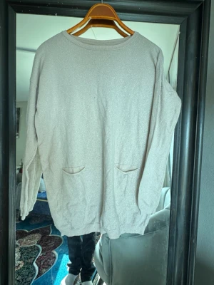 Beige oversized tröja med fickor - En beige oversized tröja med två små fickor framtill. Tröjan har rund halsringning, långa ärmar och är gjord i ett mjukt, stickat material. Perfekt för en chill och avslappnad stil.