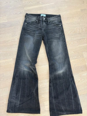 Svarta utsvängda jeans från Revice - Säljer ett par svarta jeans från Revice med utsvängda ben och slitna detaljer. Jeansen har klassisk femficksmodell, knappgylf och cool tvätt som ger en vintagekänsla. Perfekta för dig som gillar retrostil och vill sticka ut.