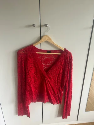 Röd omlottblus i spets - Snygg röd omlottblus i transparent spets med djup v-ringning och långa ärmar. Blusen har ett feminint snitt och är perfekt för att skapa en trendig look. Materialet är lätt och luftigt med fina spetsdetaljer. Blus är aldrig använd❤️