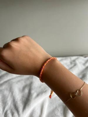 Färgglatt flätat vänskapsarmband - Säljer ett handgjort vänskapsarmband i flätad design med färgerna orange, rosa och gult. Armbandet är gjort av tunna bomullstrådar och justerbar .Perfekt accessoar för dig som gillar färg och en personlig touch.💕