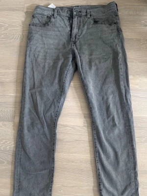 Grå raka jeans från Levis 502  - Säljer ett par grå Levis jeans med rak passform och klassisk femficksdesign. Jeansen har bälteshällor, knappgylf och är tillverkade i ett mjukt denimtyg. Passar perfekt till en avslappnad stil och är lätta att matcha med olika plagg. Storlek 32/32