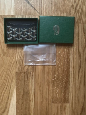 Svart mönstrat kortfodral - Stilrent svart kortfodral med vitt och grått grafiskt mönster. Kommer i en grön box med logga på locket. Perfekt för kort och har en smidig, tunn design. Materialet ser ut att vara konstläder eller canvas.