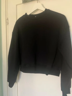 Svart sweatshirt från Divided - En enkel svart sweatshirt från Divided i storlek XS. Tröjan har rund halsringning, långa ärmar och ribbade muddar vid ärmslut och nederkant. Perfekt basplagg att matcha med jeans eller kjol.