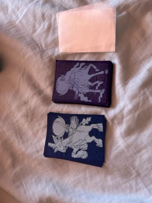 Pokémon kort sleeves med motiv - Två högar Pokémon kort sleeves med motiv av legendariska Pokémon i lila och blå färg. Ena högen har ett vitt motiv av en hästliknande Pokémon på lila bakgrund, den andra har en liknande design på blå bakgrund. Perfekt för att skydda samlarkort.